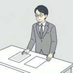 机の上に紙が二枚。左は行が書かれ、右は白紙。会社員が一人、左の紙を見ている